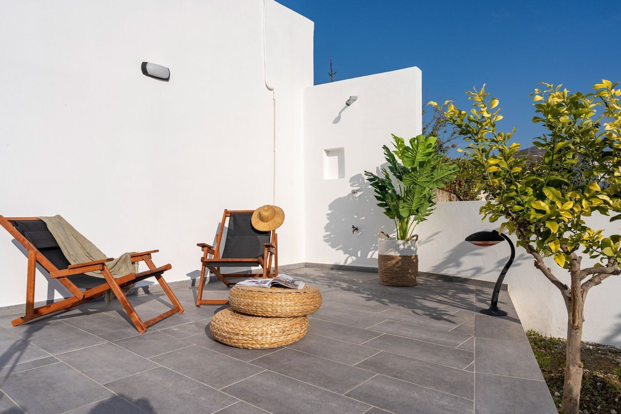 Une terrasse avec deux fauteuils de jardin en bois, un panier tressé et une plante en pot.