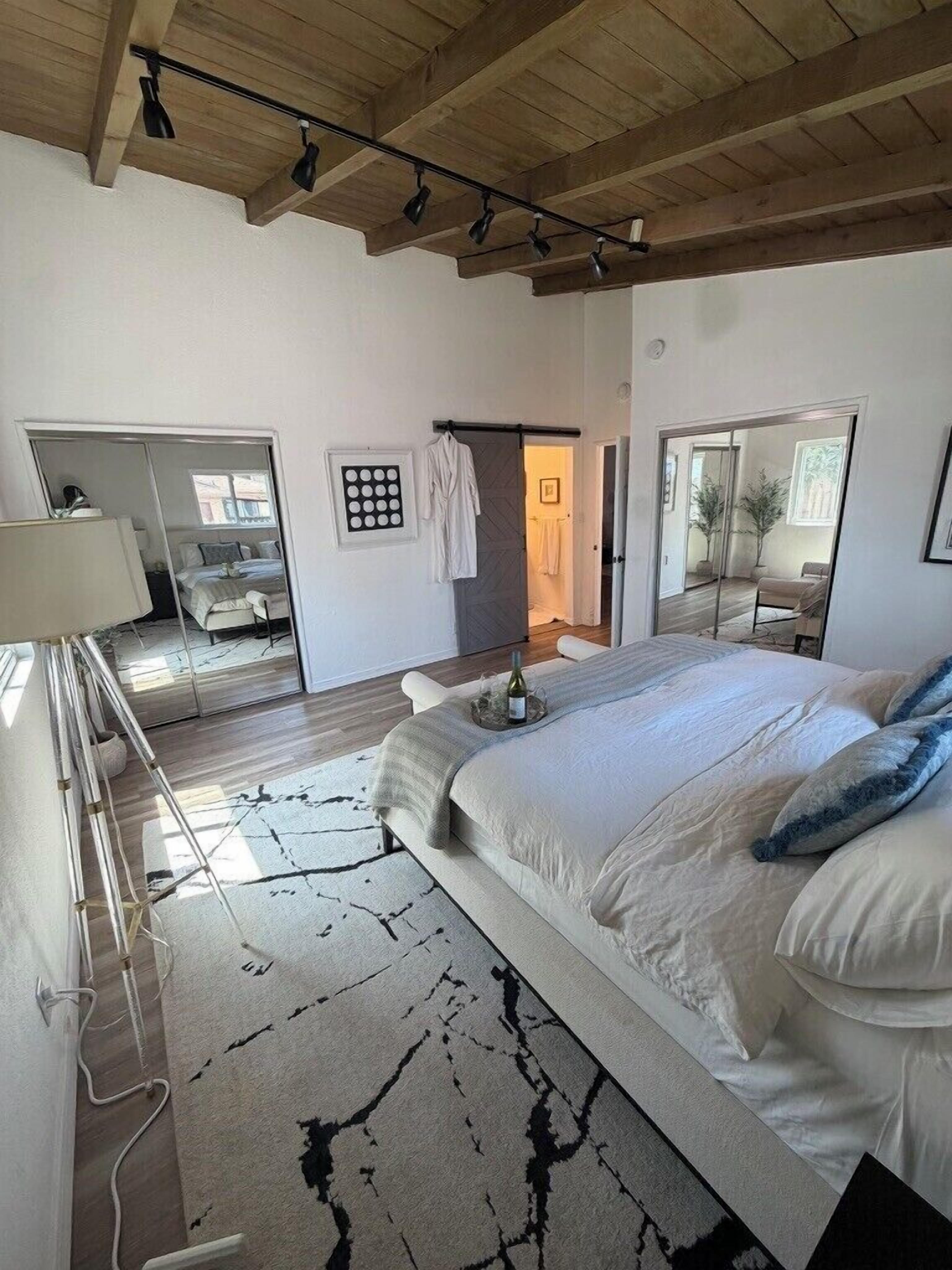 A bedroom with a large bed, a mirror, a bedside table, and a wardrobe.