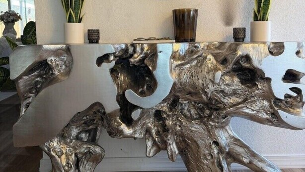 Una reception con uno specchio rotondo, due piante in vaso e un'originale scultura in legno.