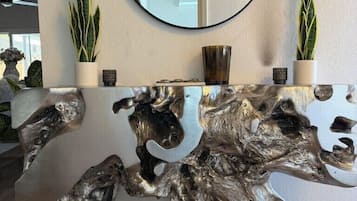 A reception desk with a round mirror, two potted plants, and a unique wooden sculpture.