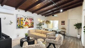 A spacious living room with a high ceiling, a sofa, two armchairs, a coffee table, and a TV.