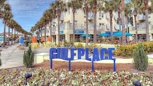 Une enseigne indiquant « GULF PLACE », avec une rangée de palmiers et un bâtiment doté de balcons en arrière-plan.