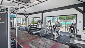 Une salle de sport équipée de matériel d’exercice, d’un tapis de course et offrant une vue sur une piscine.