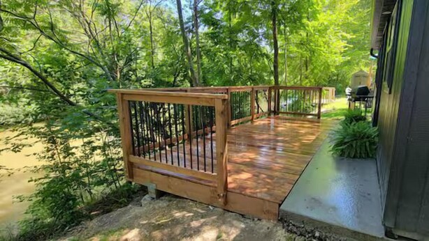 A wooden deck with a railing, a grill, and a building in the background. - Otter's Edge Estates (Vienna)