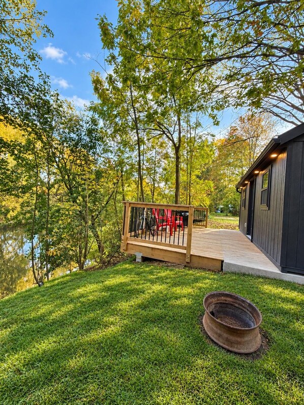 A wooden deck with a railing, a small pond, and a building with a dark exterior.