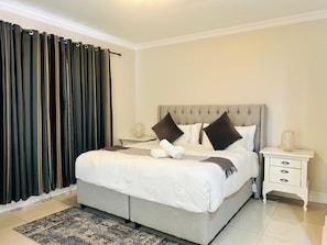 Une chambre à coucher avec un grand lit, une table de chevet, une commode et une fenêtre avec des rideaux.