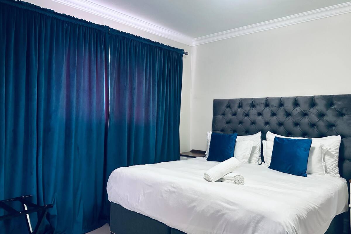 Une chambre d’hôtel avec un grand lit, des rideaux occultants et une tête de lit capitonnée.