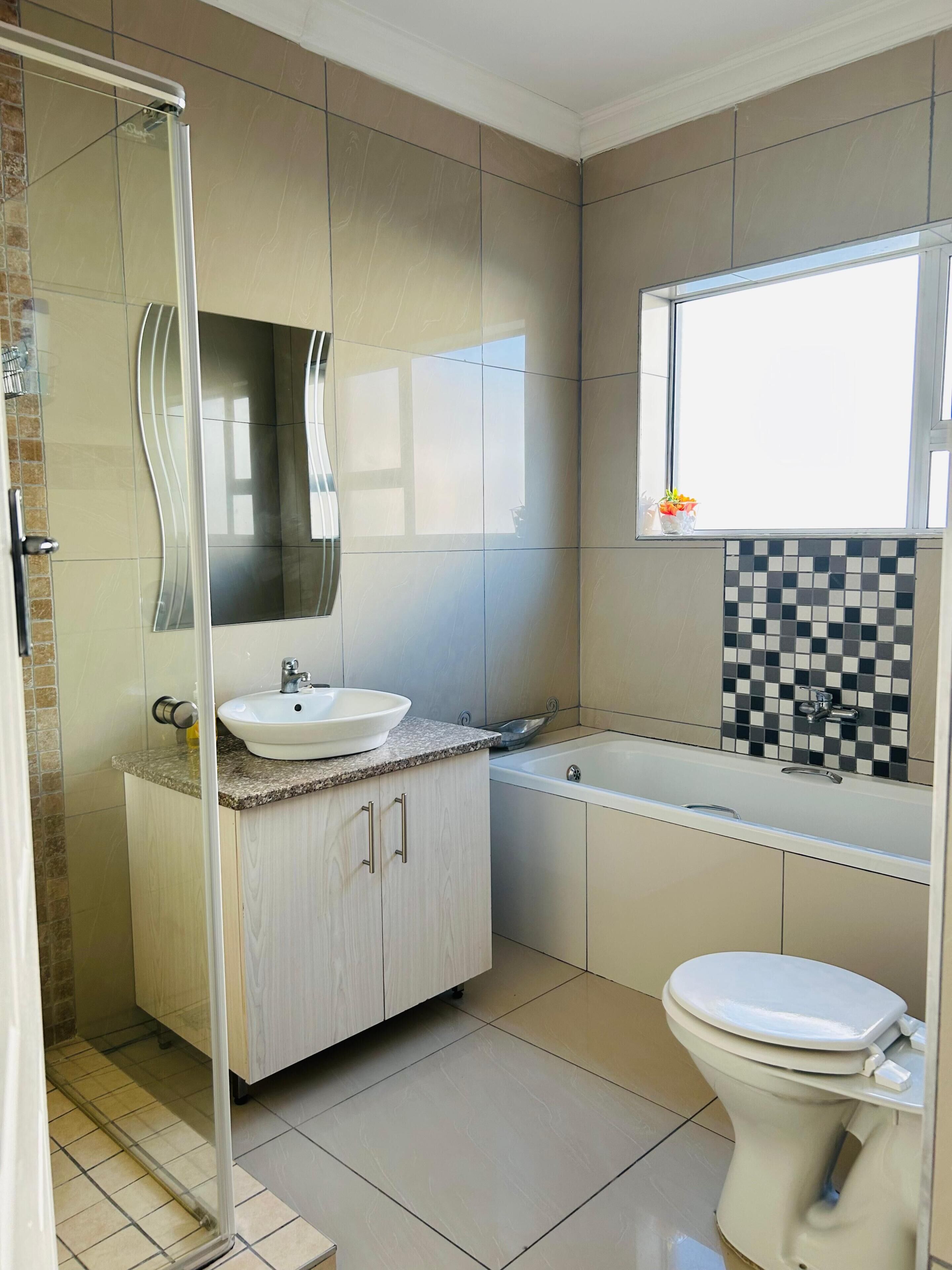 A bathroom with a shower, sink, and toilet, featuring a tiled floor and a window.