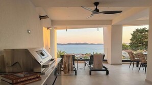 Un salón moderno con vista al mar, un ventilador de techo y una parrilla.