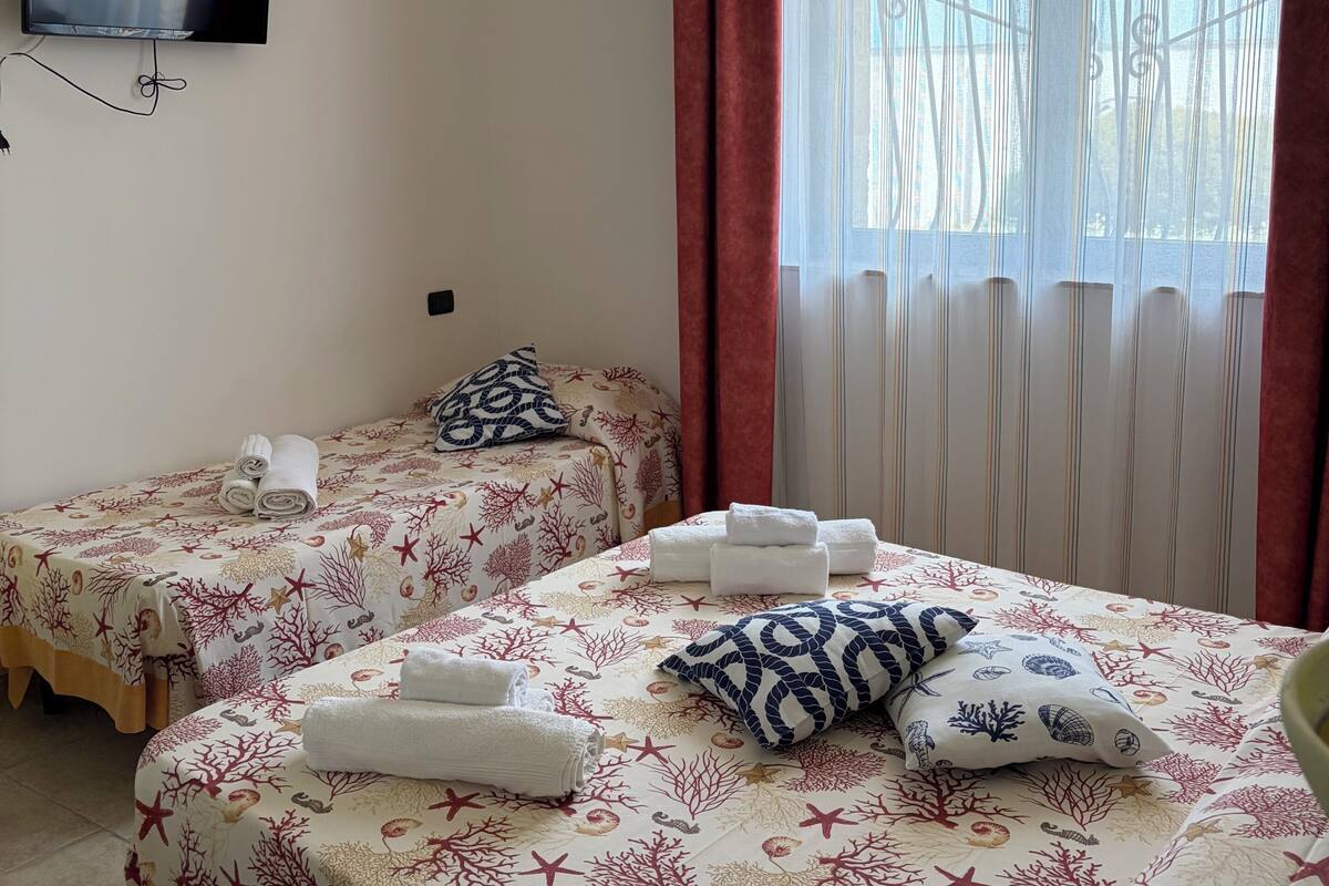 Habitació d'hotel amb dos llits, una televisió i una finestra amb cortines.