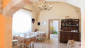 Un espace repas comprenant des tables, des chaises, un lustre, un bar avec des bouteilles et une arche en pierre.