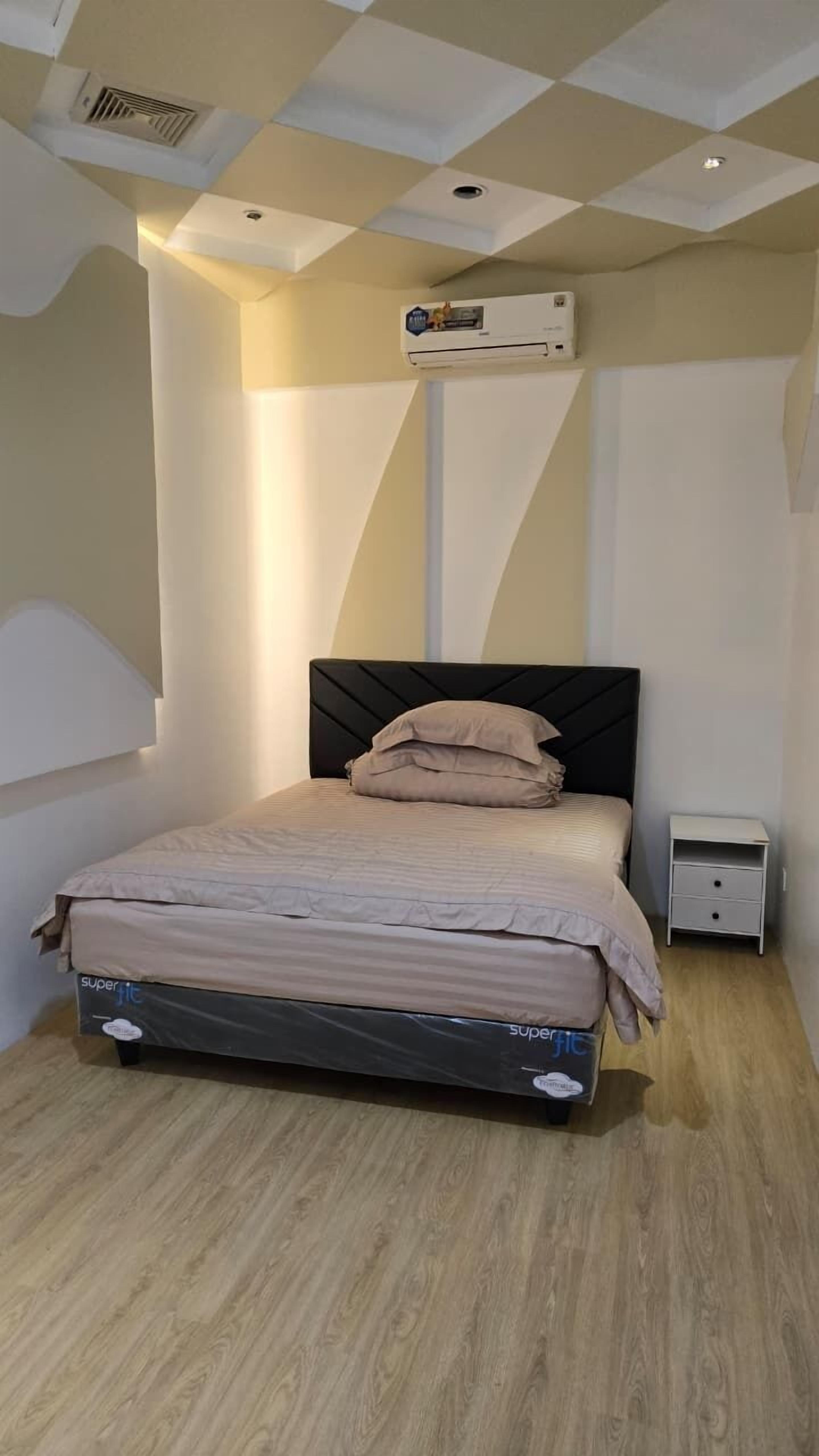 A bedroom with a bed, a nightstand, a wall-mounted air conditioner, and a ceiling with recessed lighting.