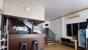 A restaurant with a wooden counter, stools, a staircase, a refrigerator, and a wall clock.
