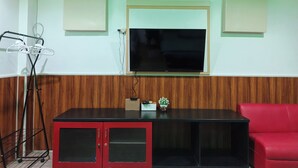 A room with a TV mounted on the wall, a red cabinet, a red couch, and a wooden panel wall.