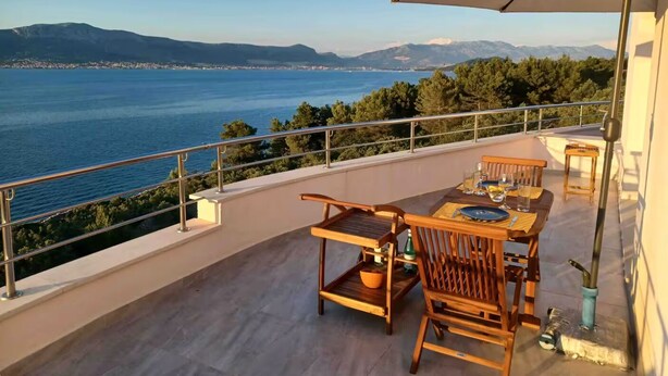 A balcony with a table and chairs, overlooking a body of water and distant mountains. - Blissful apartment by the sea with panoramic view (Slatine)