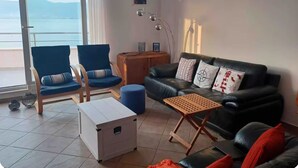 A living room with a black leather sofa, two blue armchairs, a wooden coffee table, and a white storage box. - Blissful apartment by the sea with panoramic view (Slatine)