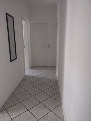 A hallway with white walls, a tiled floor, and a white door at the end. - Renovated Old Town Heidelberg 85sqm (Heidelberg)