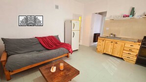 A living room with a sofa, a coffee table, a kitchen area with wooden cabinets, and a refrigerator.