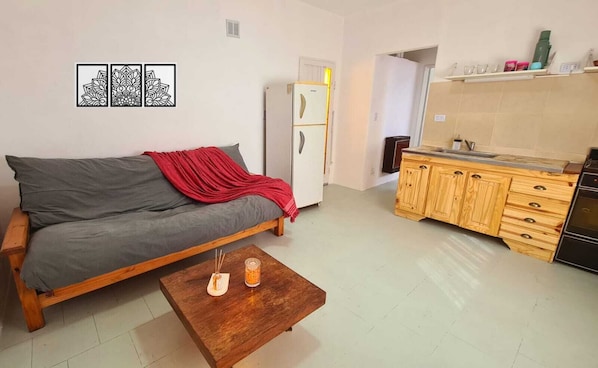 A living room with a sofa, a coffee table, a kitchen area with wooden cabinets, and a refrigerator.