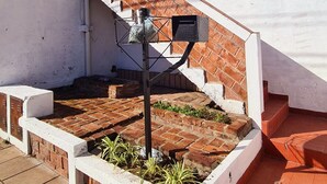 A white building with a brick staircase, a metal structure on the ground, and a small garden area.