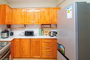 A kitchen with wooden cabinets, a refrigerator, a microwave, a toaster, and a stove. - TANZANITE APARTMENT (Kwa Mchina Mwanzo)
