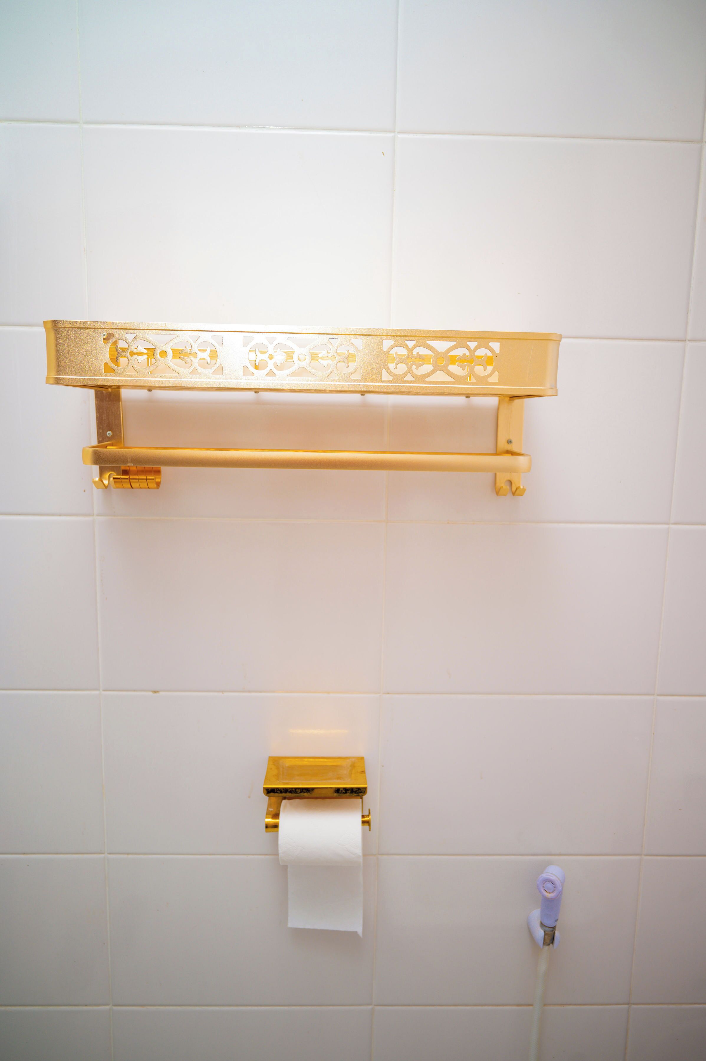 Un bany amb una barra de tovalloles daurada, un suport de paper higiènic i un airejat fixat a la paret.