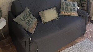 En mørk sofa med to puder, hvoraf den ene har teksten 'CHILL & RELAX', op ad en væg med struktur og et indrammet verdenskort.
