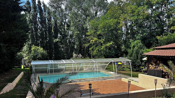 En swimmingpool med et glasmiljø, omgivet af træer og et overdækket opholdsområde.