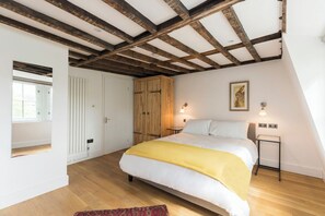 Ein Schlafzimmer mit Holzbalkendecke, einem Bett mit gelber Decke, einem Nachttisch und einem Fenster.