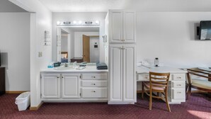 A hotel room with a vanity, mirror, and lighting. There is a desk with a chair and a TV mounted on the wall. - Auburn Inn South (Auburn)