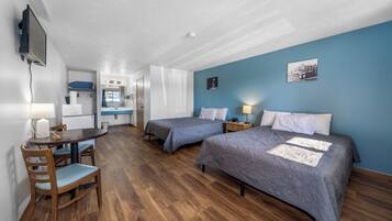 Habitación de hotel compacta con dos camas, un escritorio y una kitchenette.