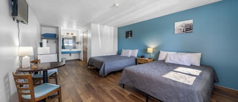 A compact hotel room with two beds, a desk, and a kitchenette.