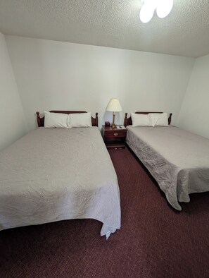 A hotel room with two single beds, a nightstand with a lamp, and a carpeted floor. - Auburn Inn South (Auburn)