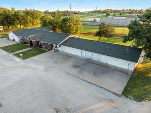 A building with a large parking area and a sports field in the background. - Auburn Inn South (Auburn)