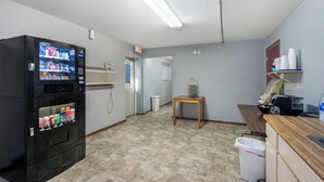 A kitchenette area with a vending machine, a trash can, a small table, and a coffee machine. - Auburn Inn South (Auburn)