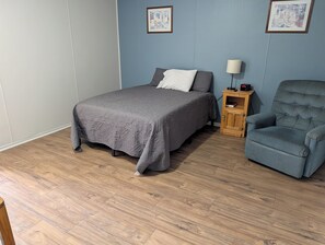 A bedroom with a bed, a chair, a nightstand, and two framed pictures on the wall. - Auburn Inn South (Auburn)