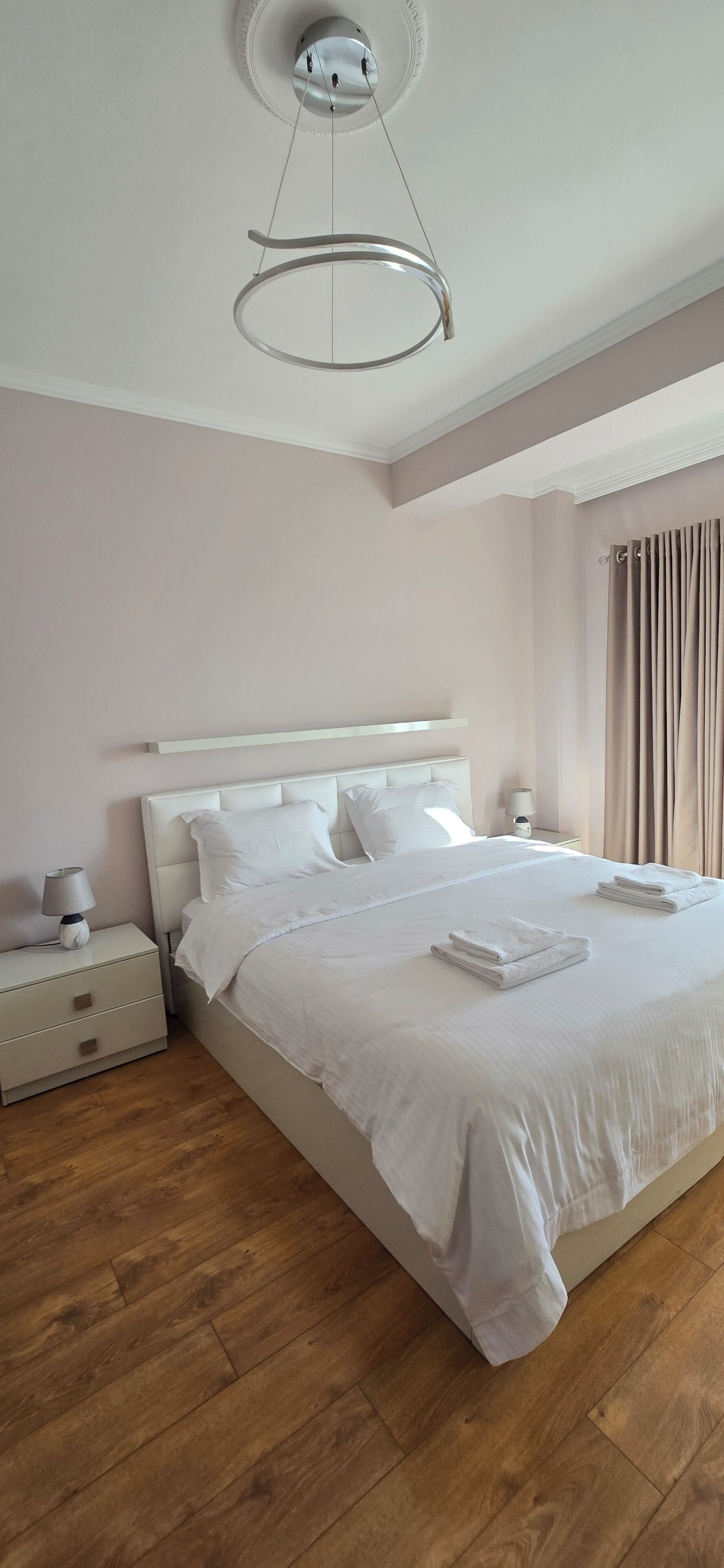 Un lit bien fait, avec du linge de lit et des serviettes blanches, une table de chevet avec une lampe et un luminaire moderne au plafond.