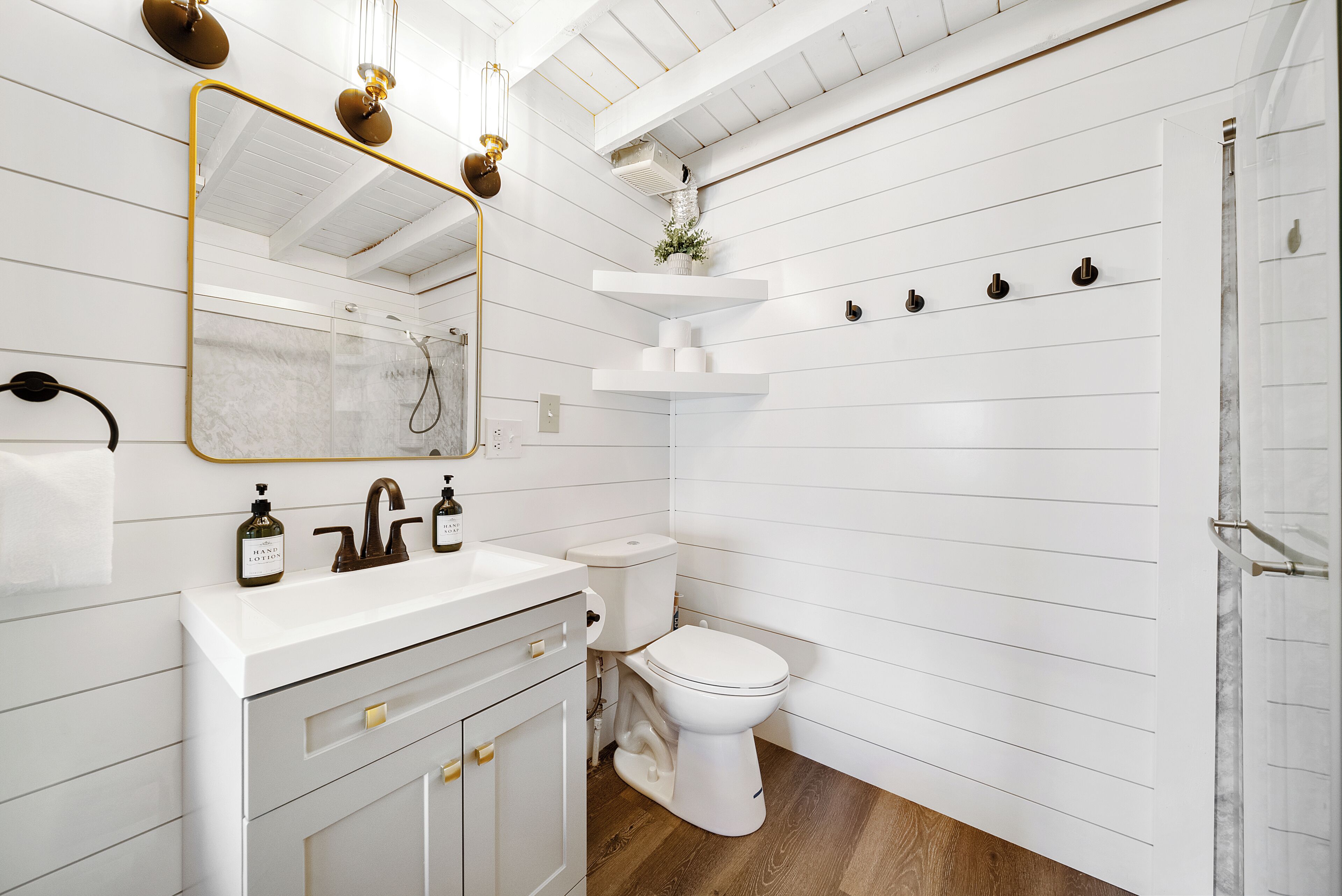 Een badkamer met een wit wastafelmeubel, een spiegel met gouden lijst, een toilet en een douchehoek.