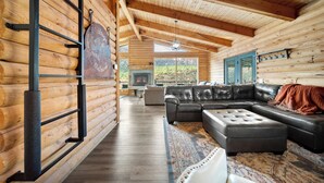 A log cabin interior with a sectional sofa, a fireplace, and a view of the outdoors. - Elevation40Zion (Apple Valley)