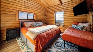 A log cabin bedroom with two beds, a large window, and a mounted TV. - Elevation40Zion (Apple Valley)