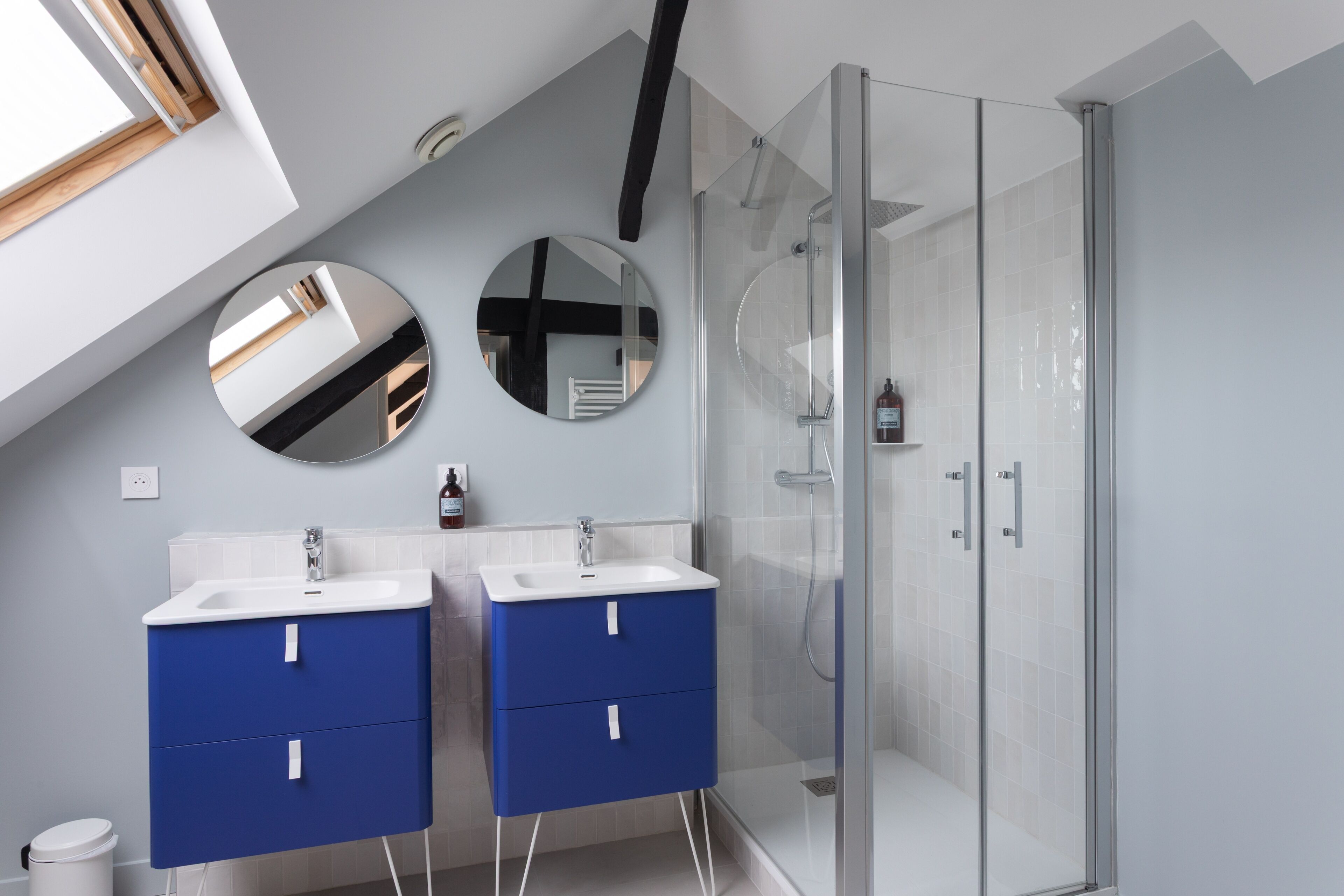 A modern bathroom with two sinks, a shower, and a skylight.