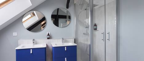 A modern bathroom with two sinks, a shower, and a skylight.