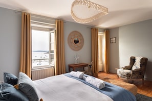 Un dormitorio con cama, una silla, una mesa, un espejo y vistas al mar.