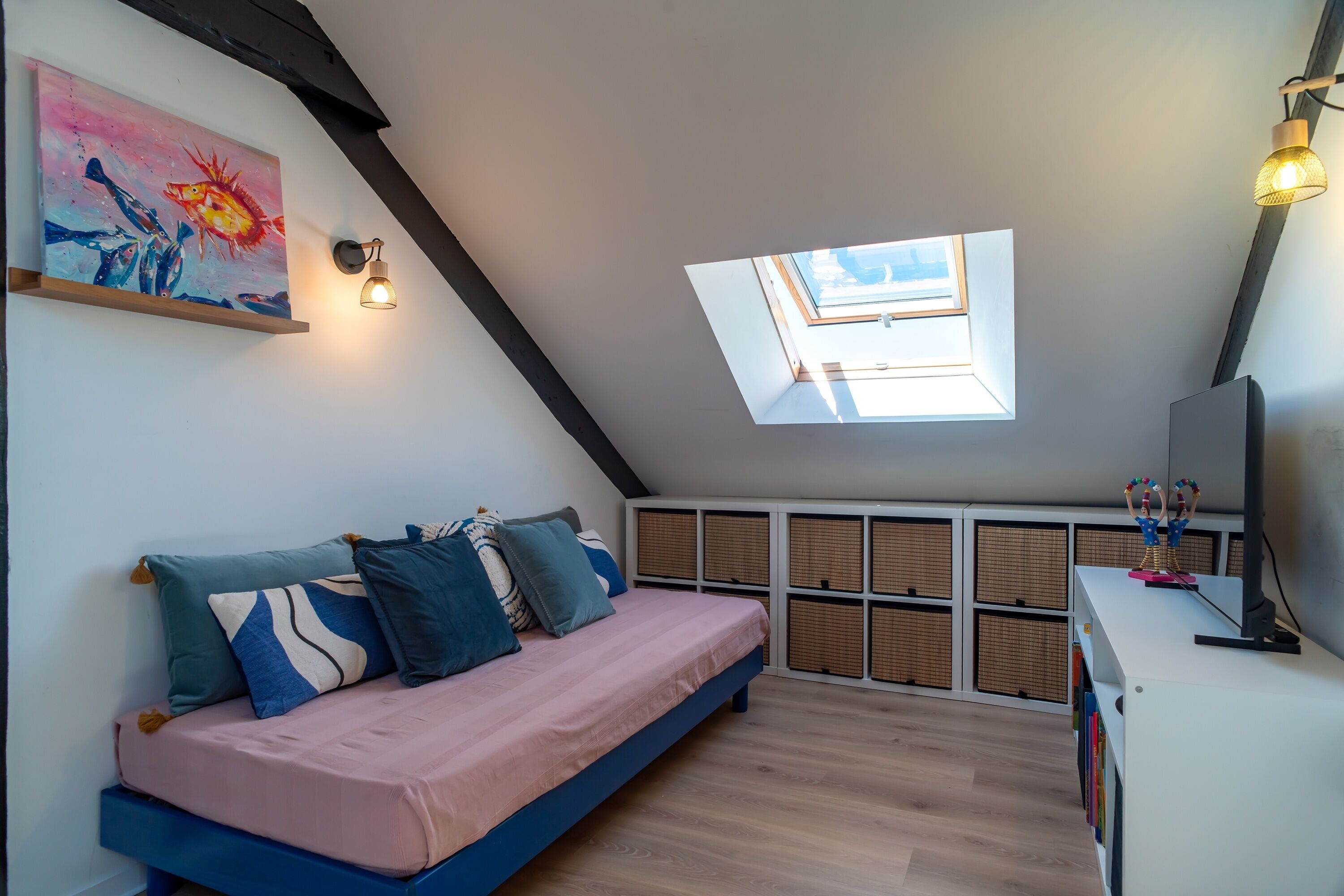 Un dormitorio tipo loft con tragaluz, una cama con almohadas, un escritorio con lámpara y un cuadro en la pared.
