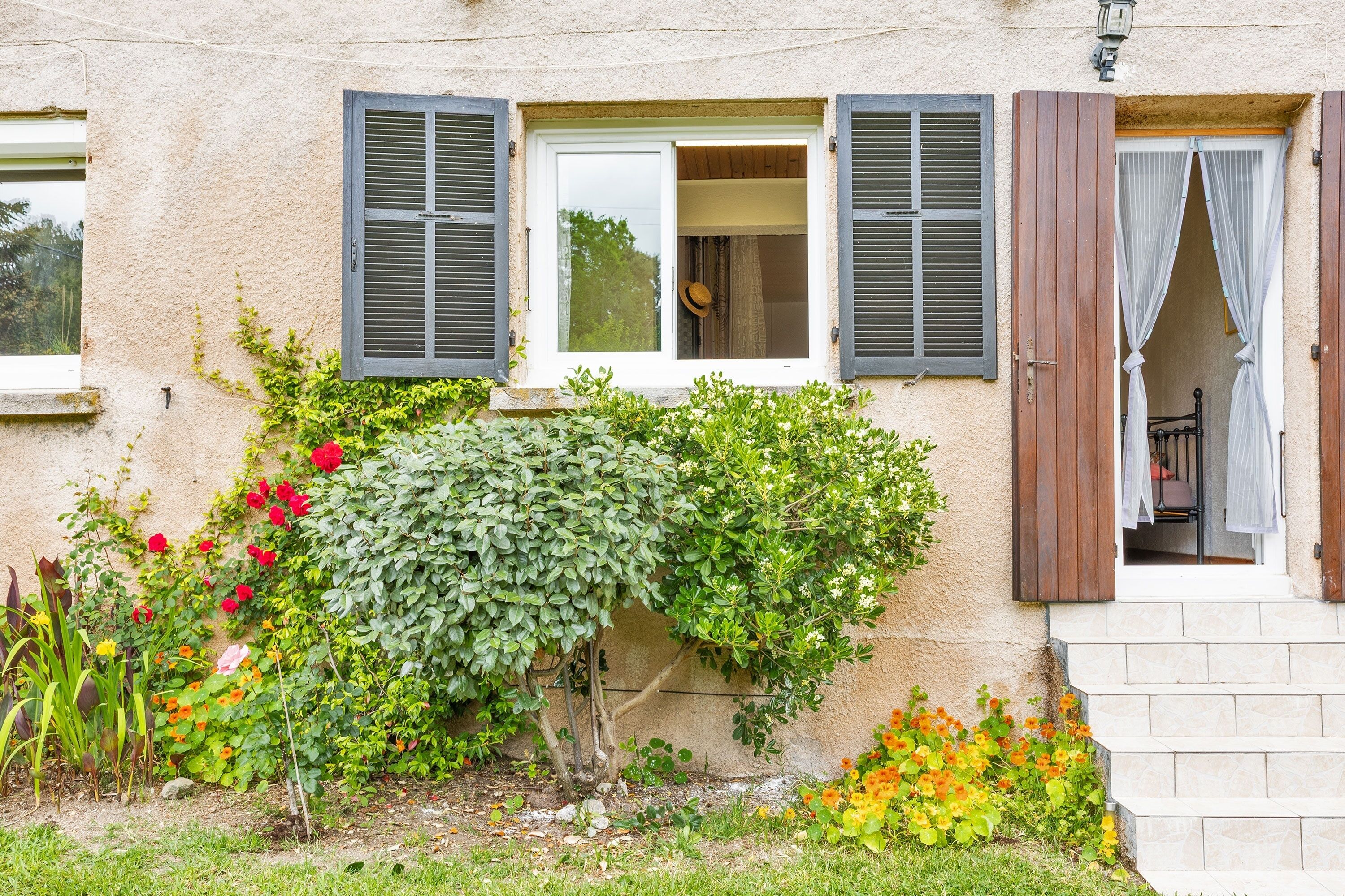 Une maison avec un jardin, une fenêtre avec des volets et une porte avec des rideaux.