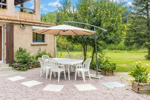 Eine Terrasse im Freien mit Tisch und Stühlen, umgeben von Kies und Topfpflanzen.