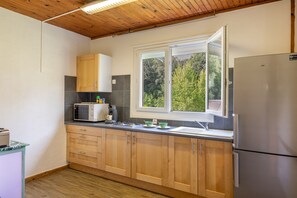 Eine Küche mit Holzausstattung, einem Edelstahl-Kühlschrank, einer Mikrowelle und einem Fenster mit Blick auf Bäume.