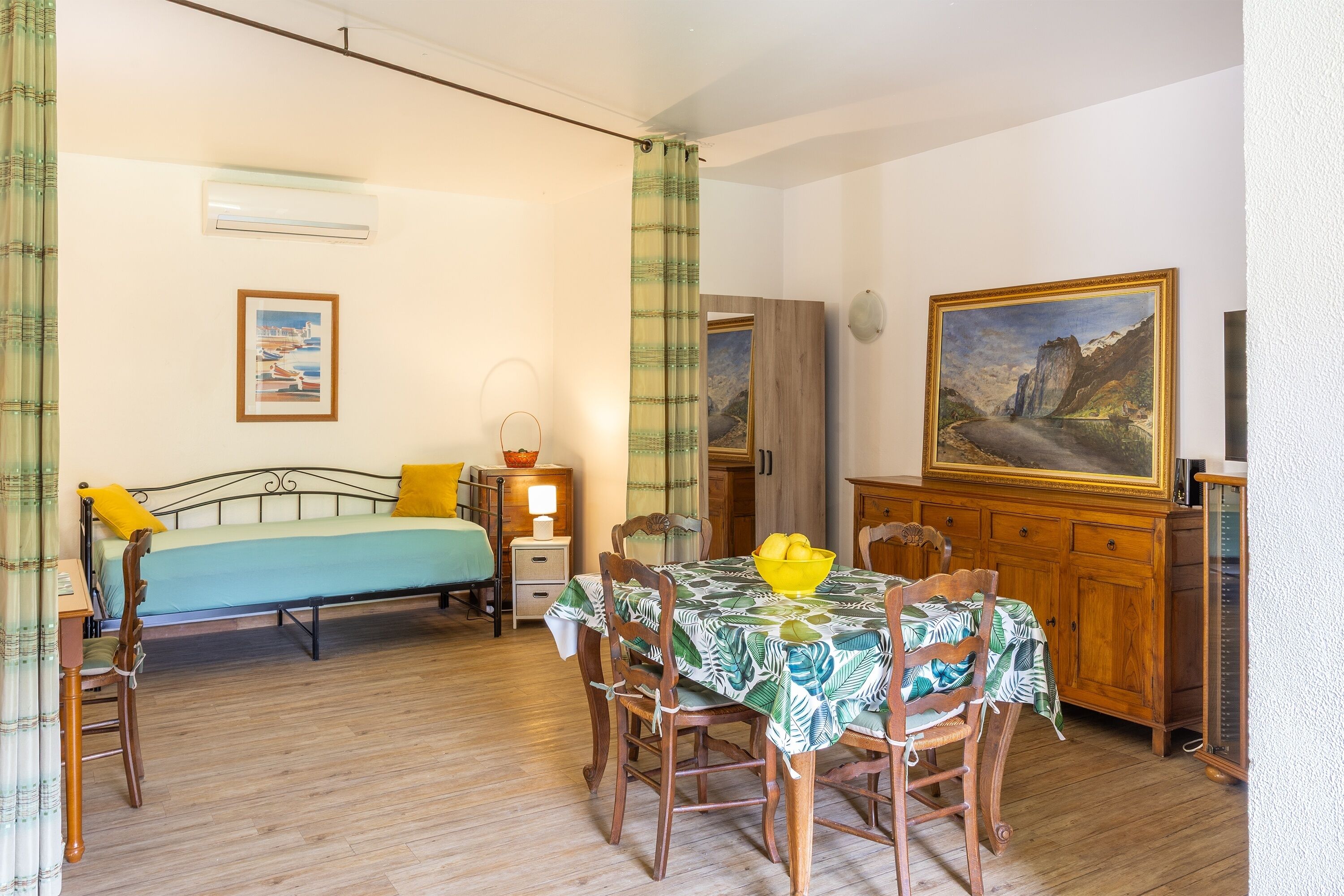 Een kamer met een bed, een eettafel met stoelen, een schilderij aan de muur en een kast.