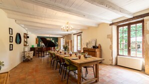 Zona pranzo con un lungo tavolo in legno, sedie e un pianoforte sullo sfondo.