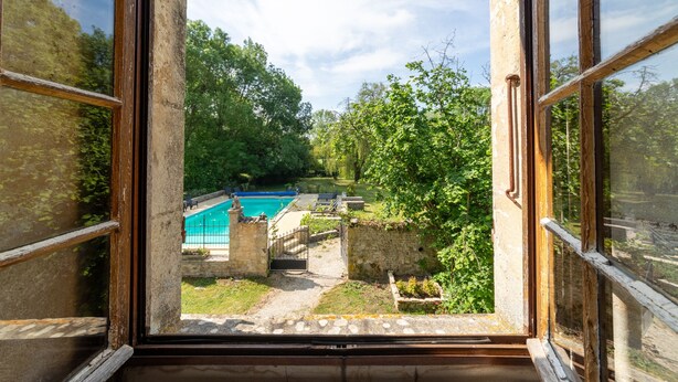 Vista dalla finestra su una piscina, pareti in pietra e vegetazione.
